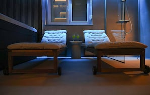 Een kamer met twee massagetafels, een raam met zonwering en een douchegedeelte.