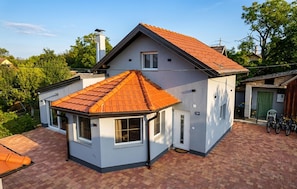 A two-story house with a red-tiled roof, a small attached garage, and a brick driveway.