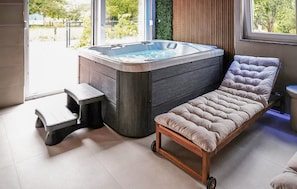 A modern bathroom with a hot tub, a step stool, and a cushioned chair.