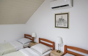 A bedroom with two single beds, a nightstand with a lamp, a wall-mounted air conditioner, and a framed picture.