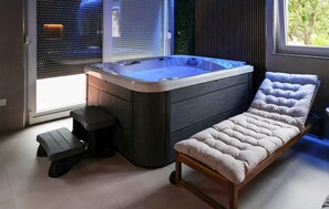 Een moderne badkamer met een bubbelbad, een bankje en een raam met zonwering.