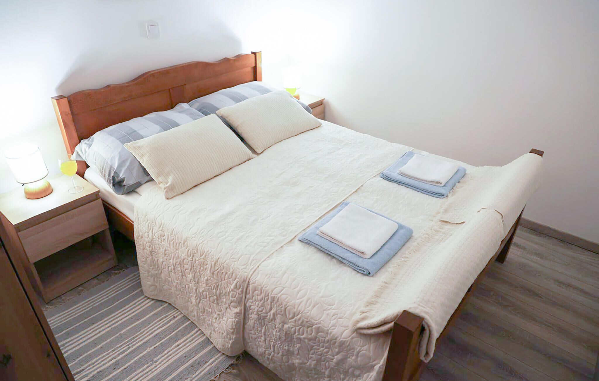 Een netjes opgemaakt bed met een houten hoofdbord, twee kussens en opgevouwen handdoeken.