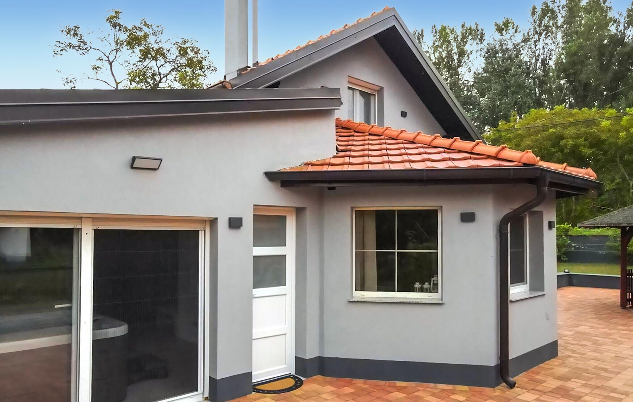 Een modern huis met een grijze gevel, een pannendak en een grote schuifdeur van glas.
