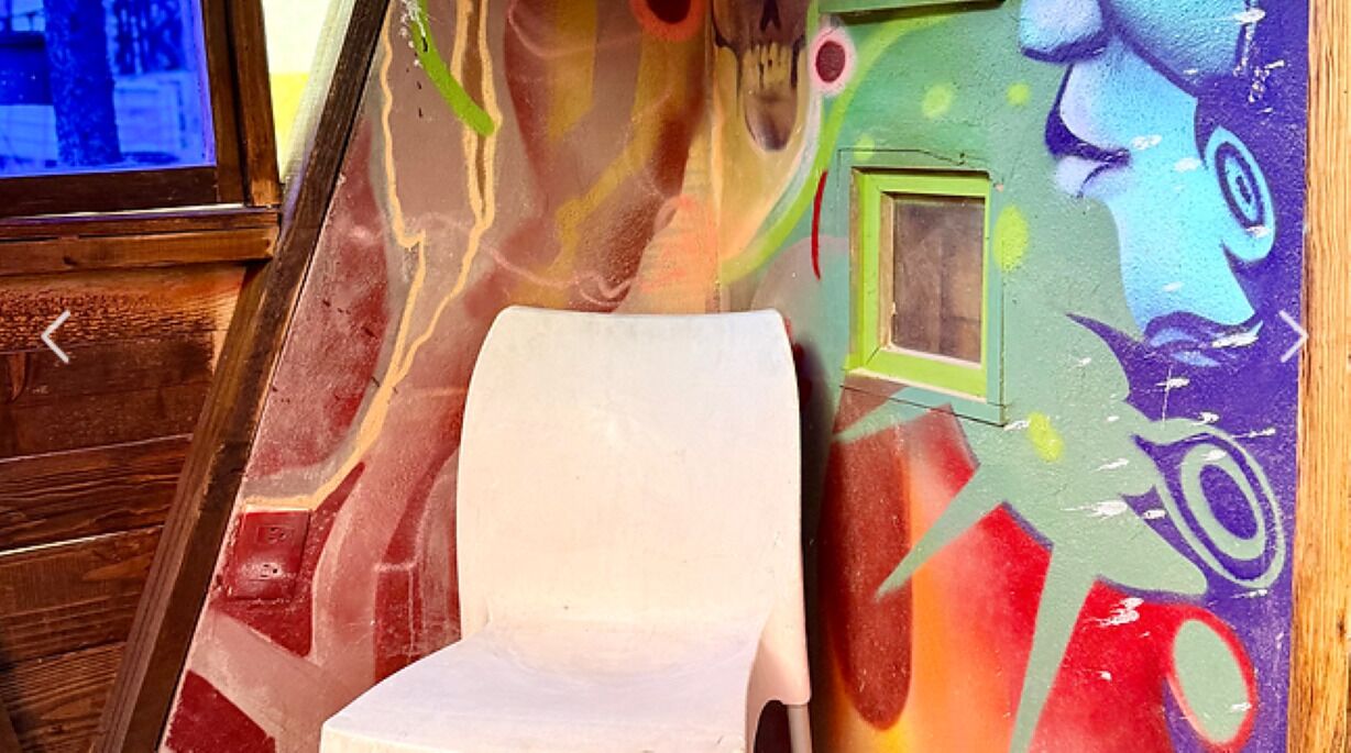 A room with a white plastic chair, a wooden door, and a colorful mural on the wall.