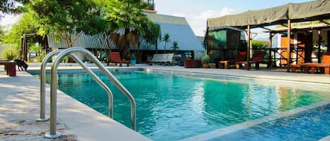 A swimming pool with a metal ladder, surrounded by lounge chairs and a covered seating area.