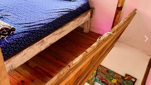A bunk bed with a blue patterned bedspread, wooden frame, and a colorful artwork on the lower bunk.