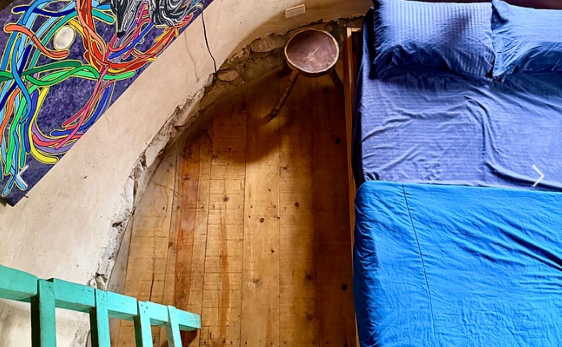 A room with a wooden floor, a blue bed, and a colorful wall decoration.