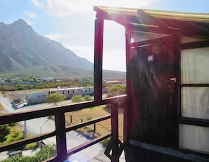 Un balcon offrant une vue sur un paysage montagneux, un bâtiment visible au loin et un ciel dégagé.