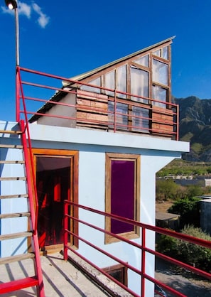 Un bâtiment à deux étages doté d’un balcon en bois, d’une rambarde en métal rouge et offrant une vue dégagée sur le paysage environnant.
