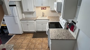 A kitchen with white cabinets, a stove, a refrigerator, and a microwave.