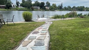 A stone pathway leading to a lakeside area with a dock and chairs.