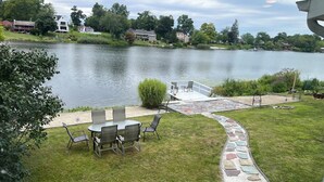 A lakeside patio with a table and chairs, a stone pathway, and a view of the lake and surrounding houses.