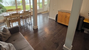 A spacious living area with a dark wood floor, a gray sofa, and a dining area with chairs and a table.