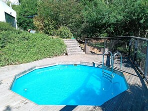 Ein Schwimmbecken mit Holzterrasse und Metallgeländern, umgeben von viel Grün.