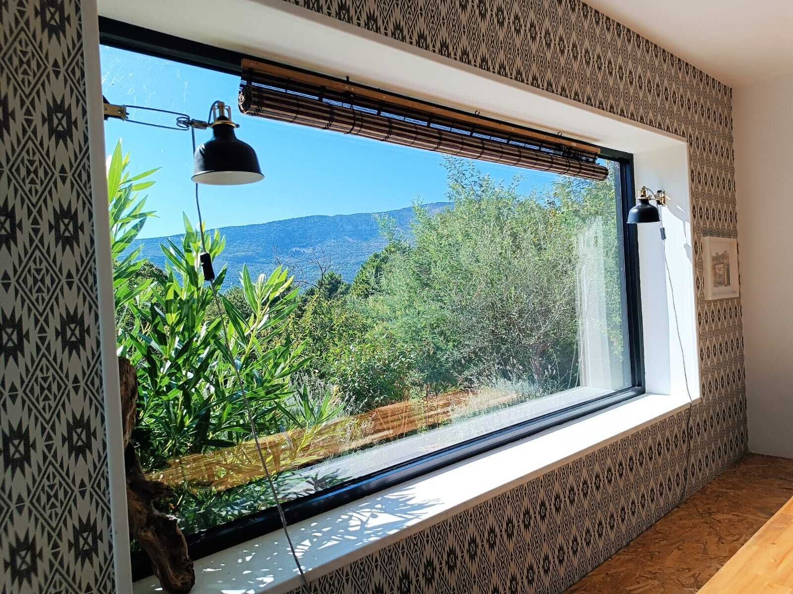 A room with a large window overlooking a garden and distant hills.