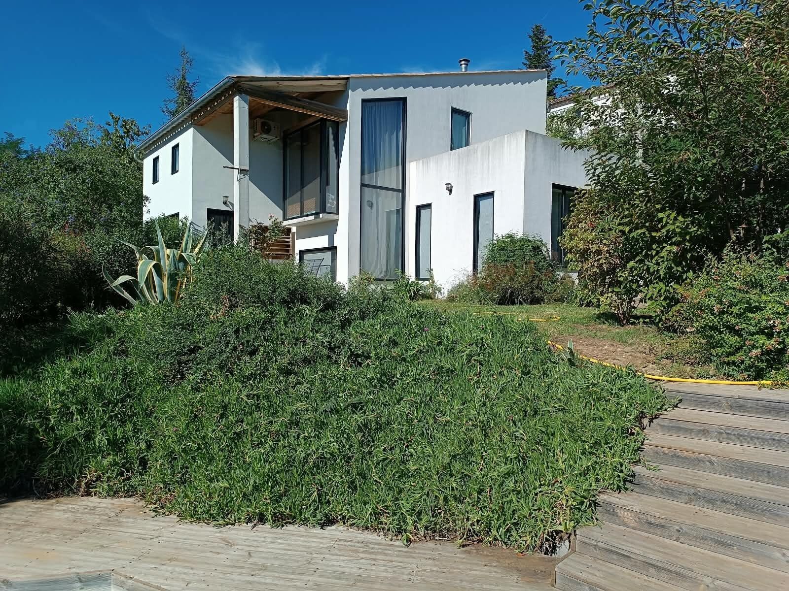 Una casa moderna de dos plantas con techo plano, ventanas grandes y un porche cubierto.
