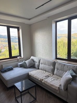 A modern living room with a sectional sofa, a small coffee table, and large windows offering a view of a landscape.