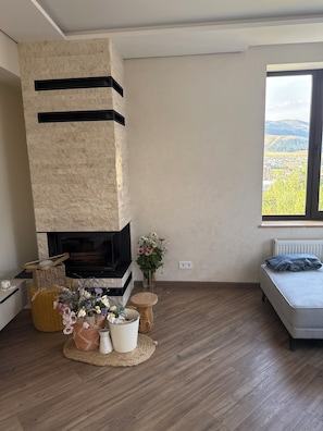 A modern living room with a stone fireplace, a sofa, a view of the outdoors, and a small table with decorative items.