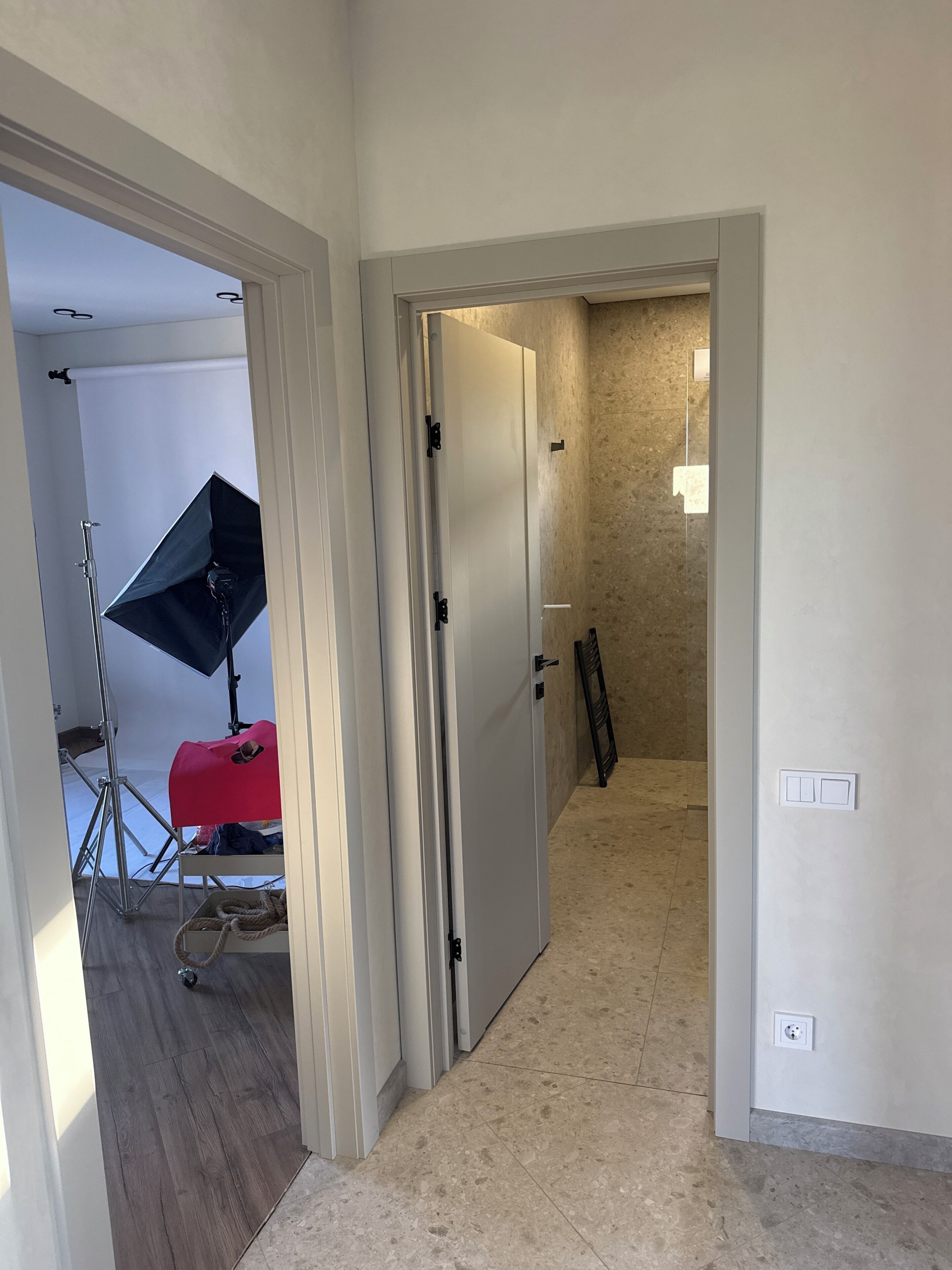 A hallway with a door leading to a room, a light fixture on the wall, and a tripod with a light stand.