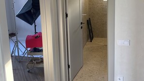 Un passadís amb una porta que dona a una habitació, una làmpada penjada a la paret i un trípode amb un estand de llum.