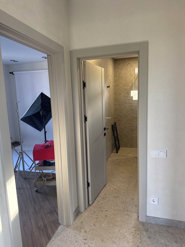 A hallway with a door leading to a room, a light fixture on the wall, and a tripod with a light stand.
