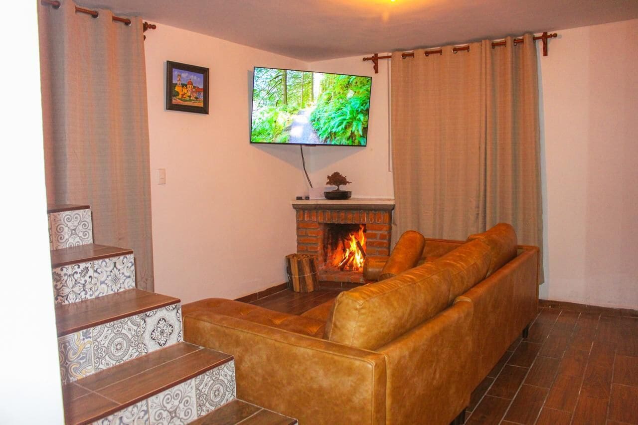 Een woonkamer met een open haard, een bank, een aan de muur bevestigde televisie en een trap met versierde tegels.