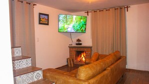 A living room with a fireplace, a sofa, a television mounted on the wall, and a staircase with patterned tiles. - Vrbo Property (La Estanzuela)