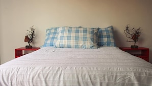 A bed with a white quilt and blue and white checkered pillows, flanked by two red nightstands with decorative items. - Vrbo Property (La Estanzuela)