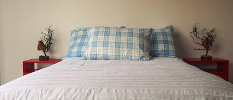 A bed with a white quilt and blue and white checkered pillows, flanked by two red nightstands with decorative items.