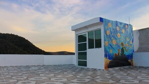 A rooftop terrace with patterned flooring, a small enclosed area with a glass door, and a wall with a colorful painting. - Vrbo Property (La Estanzuela)
