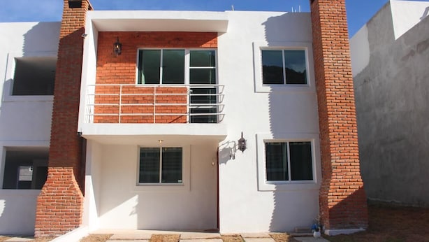 A two-story residential building with a white facade, red brick chimneys, and a balcony on the upper floor. - Vrbo Property (La Estanzuela)