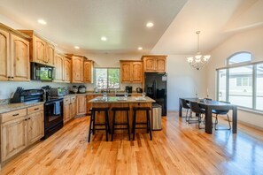 A spacious kitchen with wooden cabinets, a central island with stools, a dining area with a table and chairs, and a large window providing natural light. - Relocation Home | Workspace, Garage, Elevator, W&D (North Salt Lake)