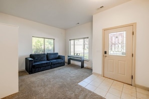 A room with a dark-colored sofa, a bench, a door with a window, and a carpeted floor. - Relocation Home | Workspace, Garage, Elevator, W&D (North Salt Lake)
