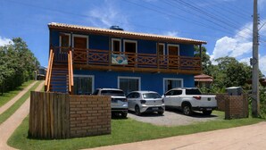 A two-story building with a balcony, a gravel driveway, and parked cars. - Pousada Santa Rosa (Imbituba)