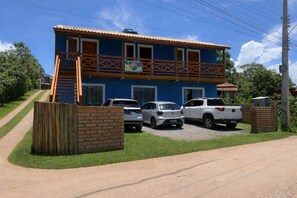 A two-story building with a balcony, a gravel driveway, and parked cars.