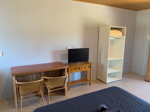 A room with a wooden desk, two wicker chairs, a television, and a white shelving unit. - Pousada Santa Rosa (Imbituba)