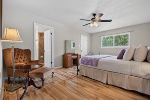 A bedroom with a wooden floor, a bed with pillows, a desk, a chair, a lamp, and a ceiling fan. - F'burg Wine Trail HQ 2BR Dog Friendly | Patio (Fredericksburg)