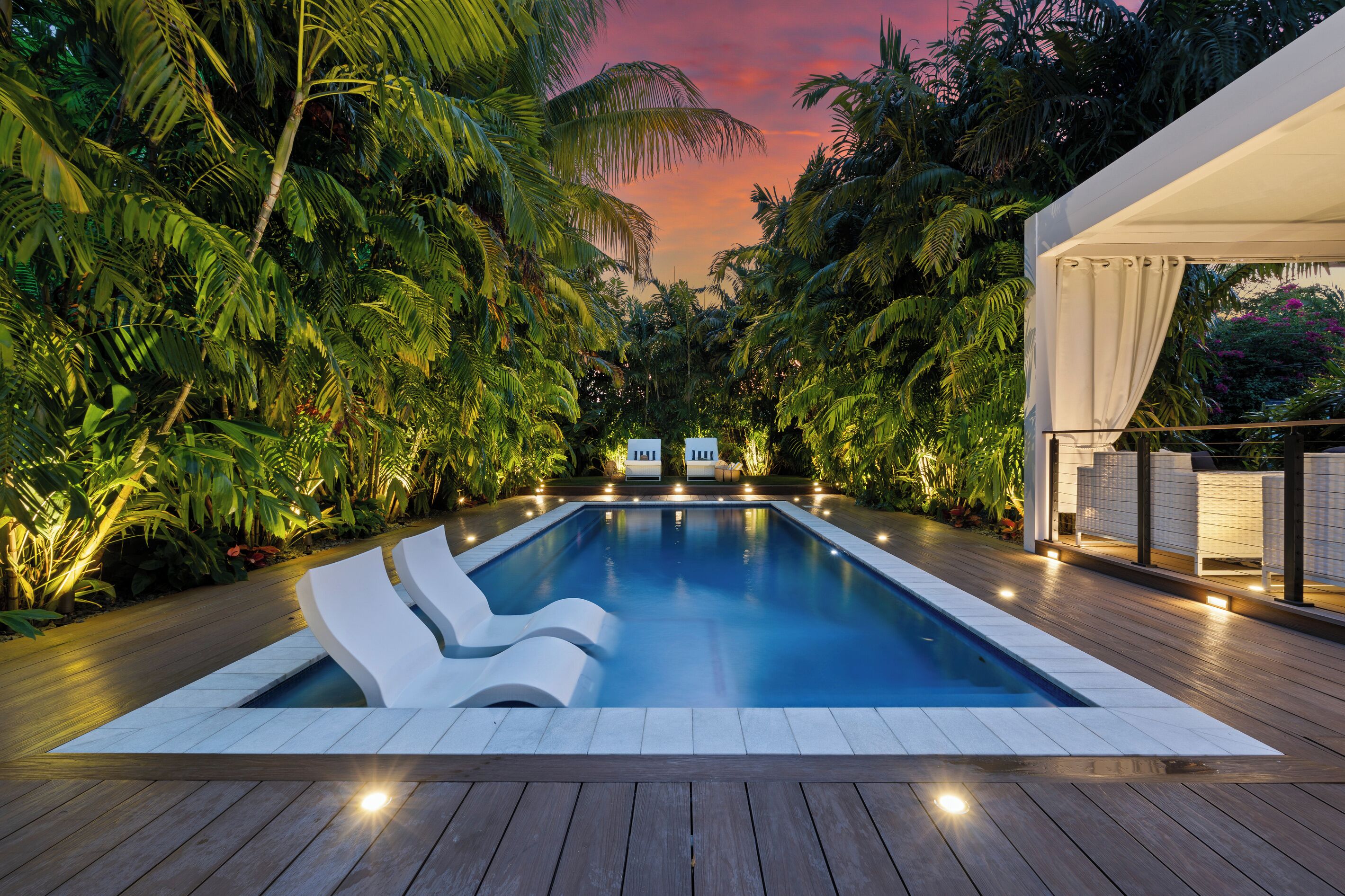 A swimming pool with lounge chairs, surrounded by dense tropical foliage, and a covered area with seating.