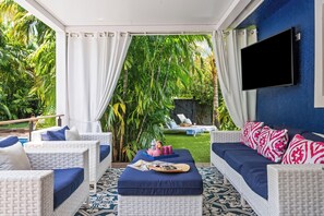 Ein Zimmer mit einer weißen Rattan-Sofagarnitur, einem blauen Hocker und einem an einer blauen Wand montierten Flachbildfernseher.