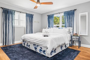 Ein Schlafzimmer mit Bett, Nachttisch, Deckenventilator und einem Fenster mit Vorhängen.