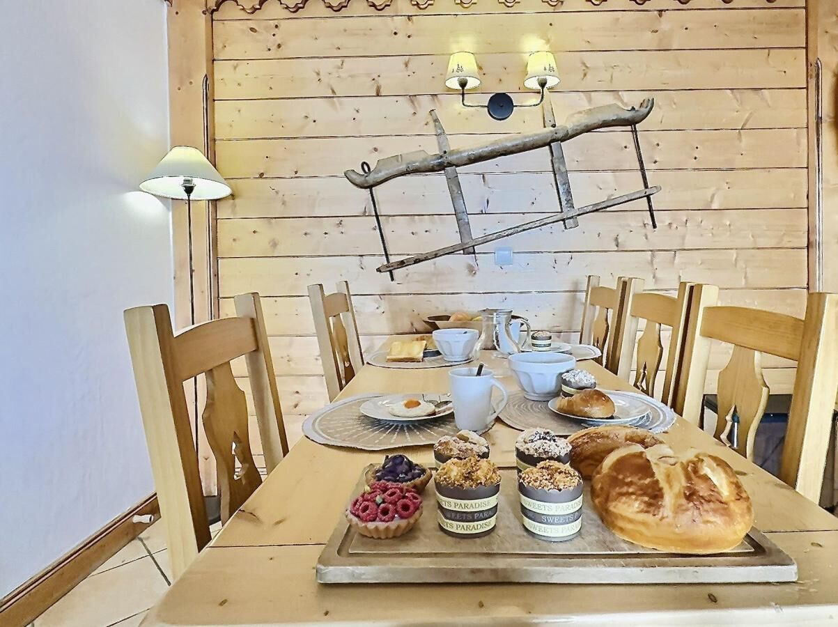 Una mesa de madera con sillas, una lámpara y una variedad de pasteles y pan.