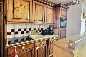 A kitchen with wooden cabinets, a tiled backsplash, and a stove. - 380m from ski slopes, 1st floor, view mountain, balcony, tv, ski locker, 59m², Tignes (Tignes)