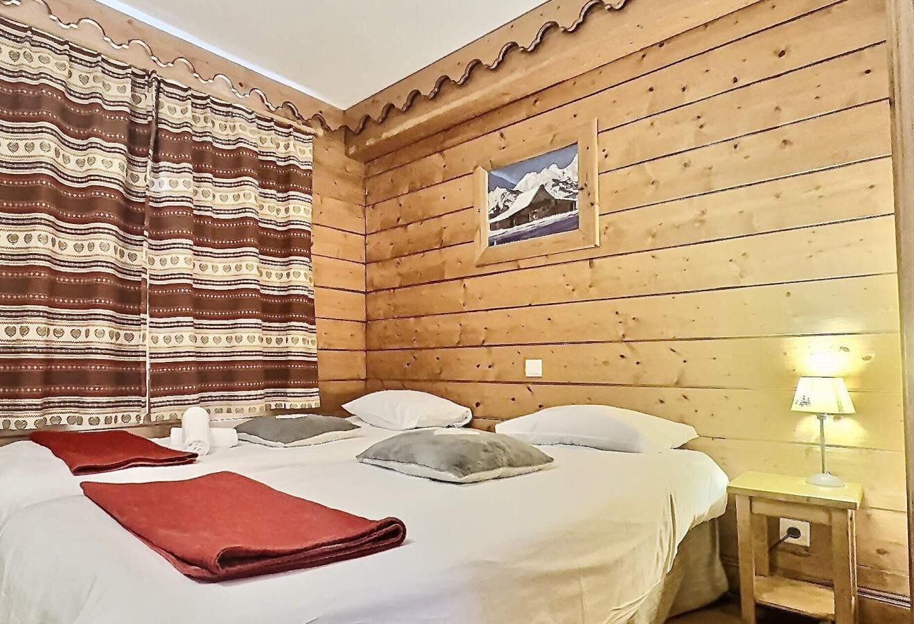 Une chambre de style cabane en bois, avec deux lits, une tête de lit en bois, un tableau au mur et une lampe de chevet.