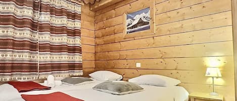 A wooden cabin-style room with two beds, a wooden headboard, a picture on the wall, and a bedside lamp.
