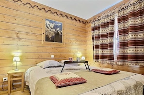 A wooden room with a bed, two bedside tables, a nightstand, a window with patterned curtains, and a painting on the wall. - 380m from ski slopes, 1st floor, view mountain, balcony, tv, ski locker, 59m², Tignes (Tignes)