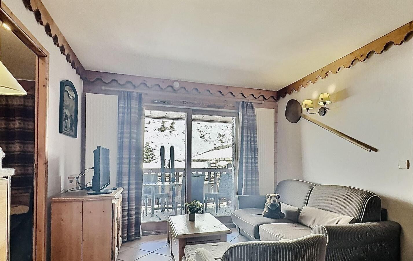 Un salon confortable avec un canapé, une petite table et un téléviseur. Il y a une fenêtre avec des rideaux et une porte qui donne sur l’extérieur.