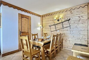 Un coin repas avec une table et des chaises en bois, un mur rustique agrémenté d’une échelle et une porte avec un cadre en bois.