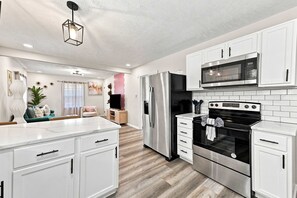 A modern kitchen with white cabinetry, stainless steel appliances, and a wooden floor.
