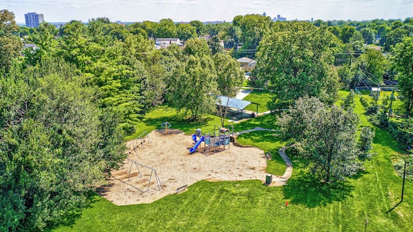 An aerial view of a park with playground equipment, a covered seating area, and surrounding greenery.
