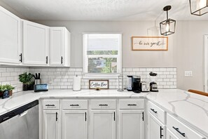 A modern kitchen with white cabinetry, a coffee bar, and a sign that reads 'be our guest.'